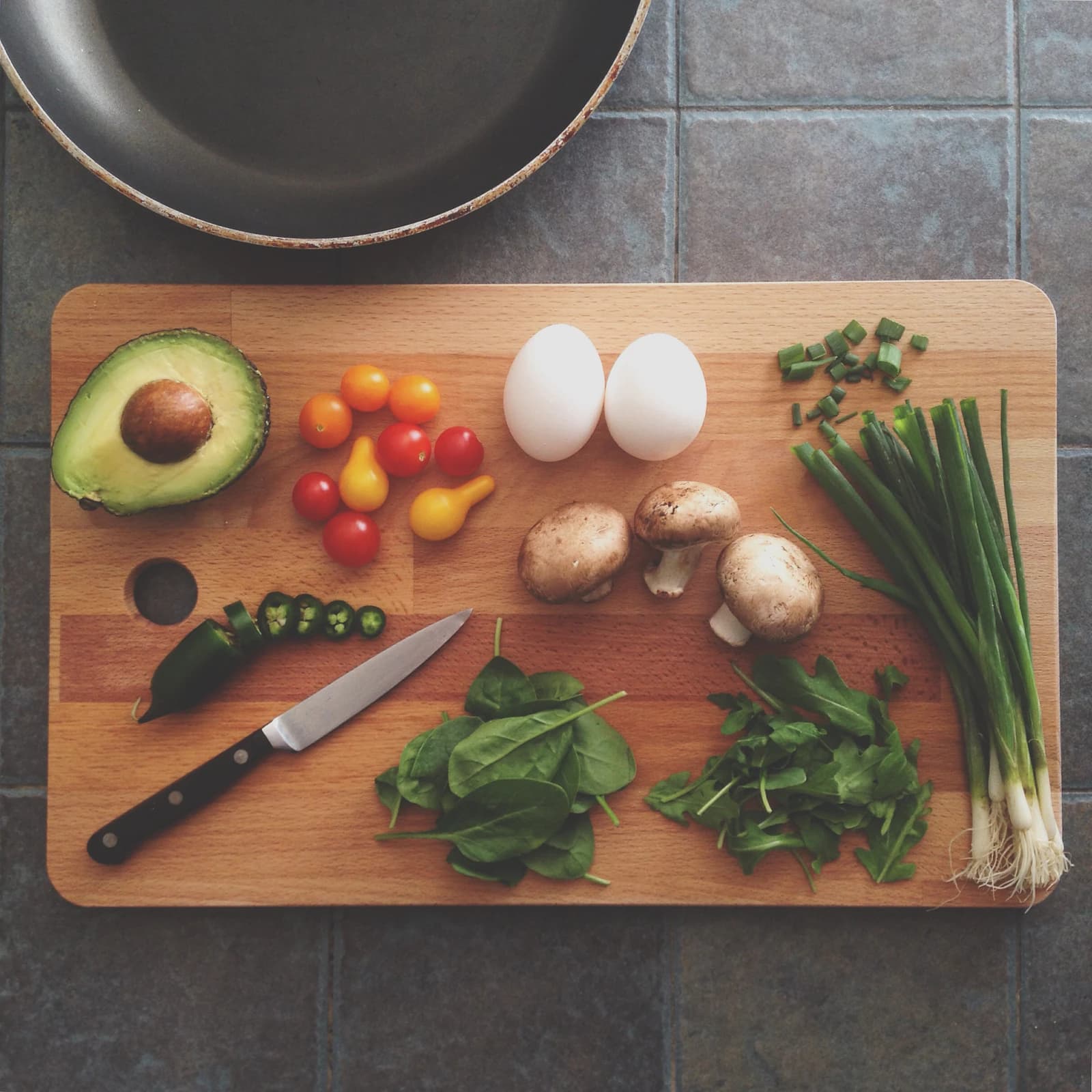 Fresh vegetables, eggs, herbs and a knife arranged on a wooden chopping board